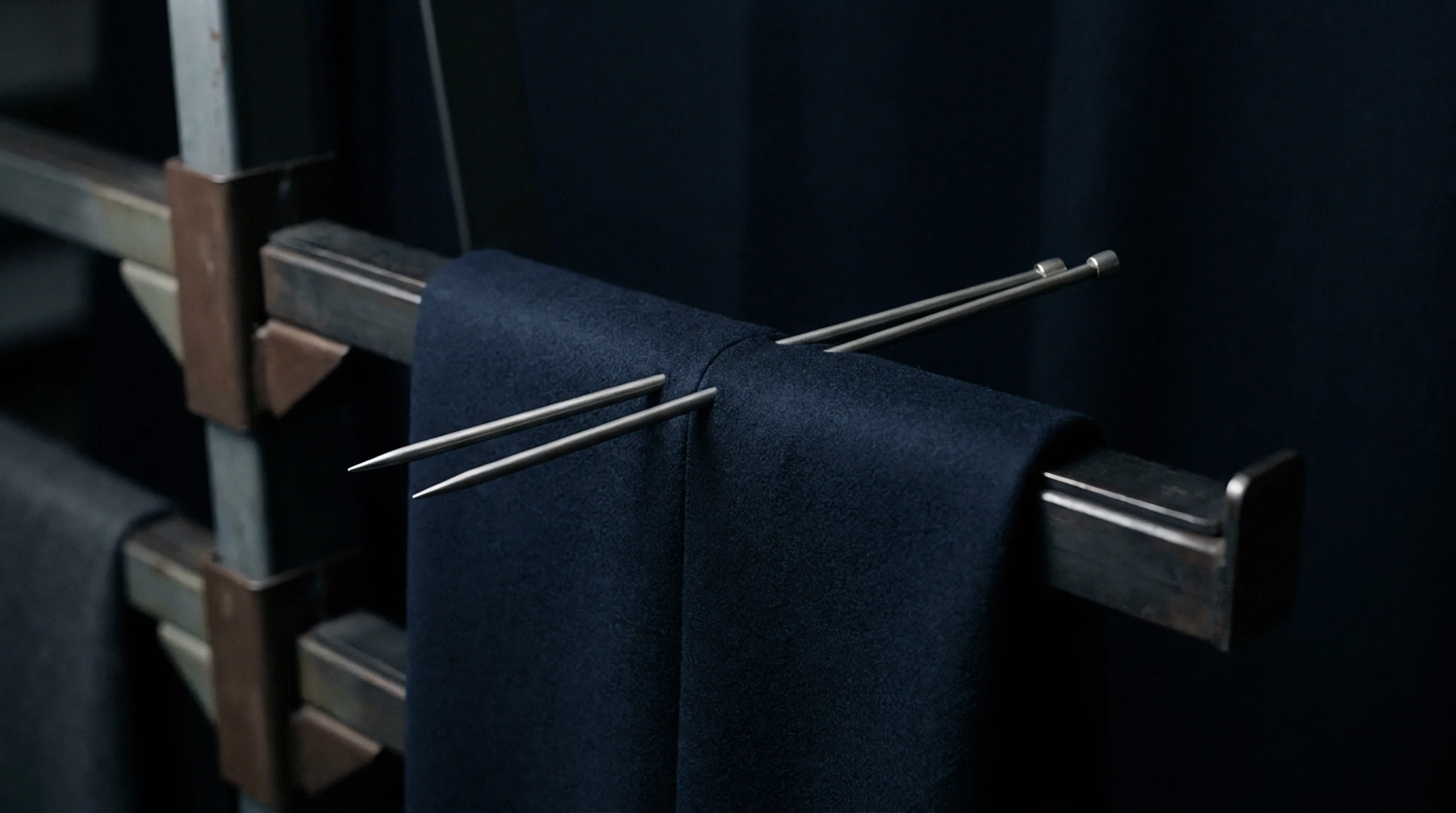 Heavy dark wool suiting fabric hangs over a brushed steel industrial rack secured with metal pins.