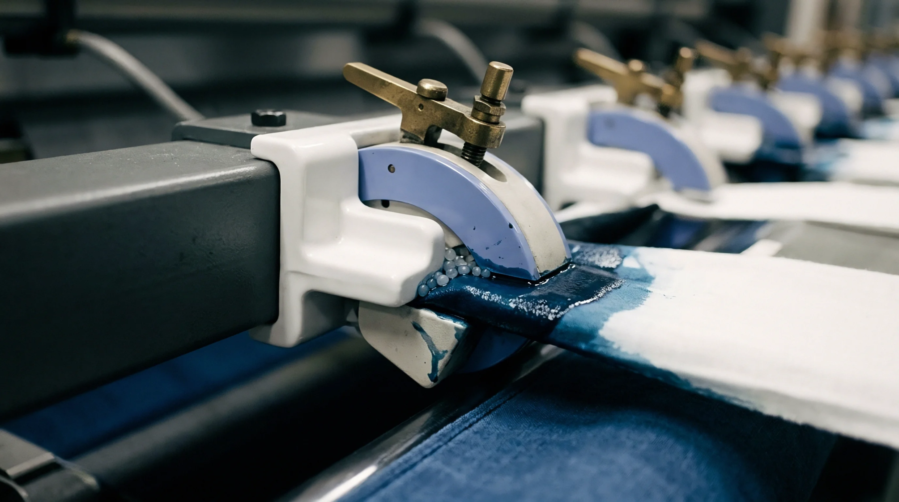 Continuous indigo dye application onto white cotton yarn ropes occurs through precision guide rollers within a heavy industrial manufacturing facility.