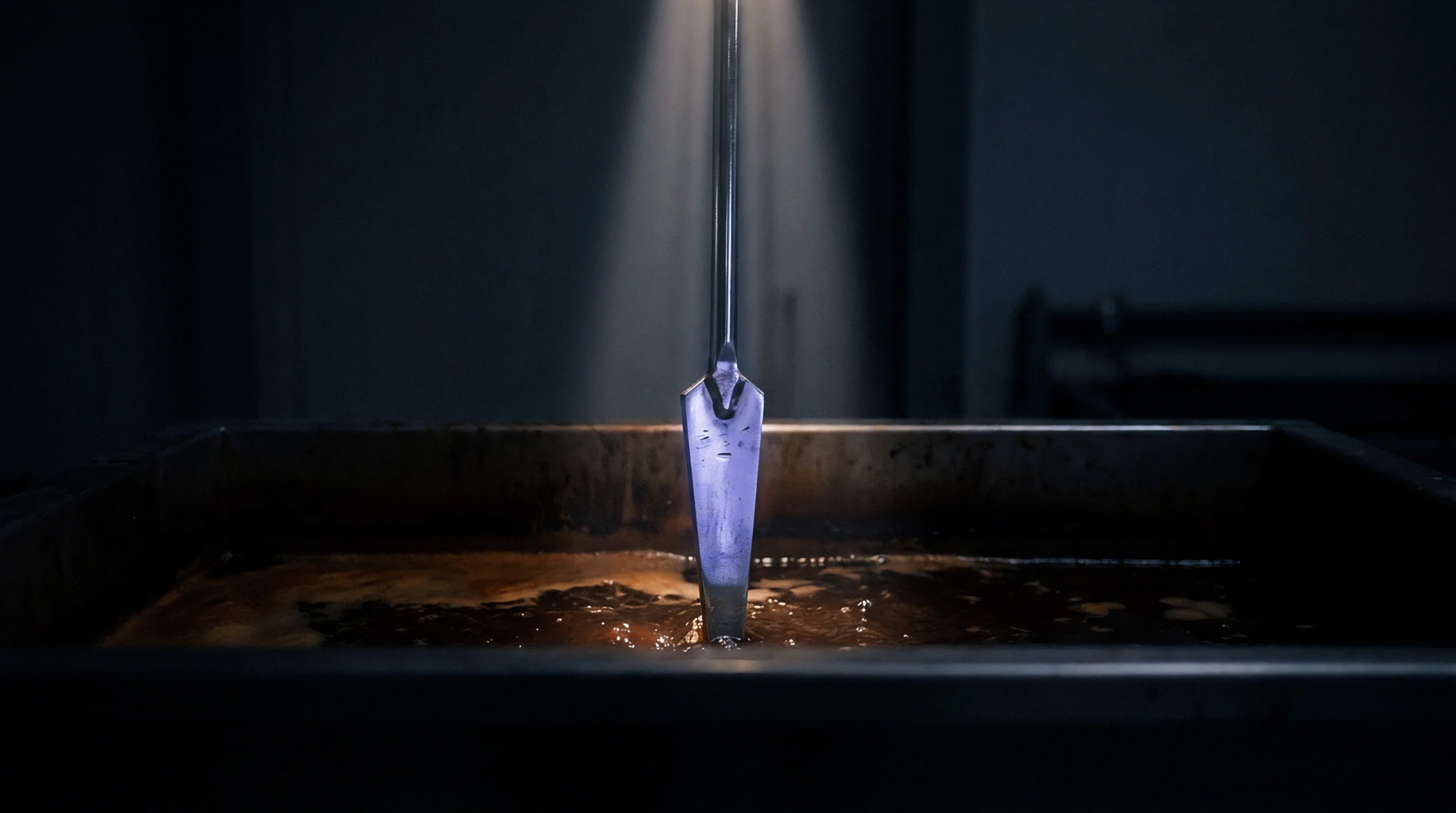 A metal immersion tool stands upright within a dark, rich liquid held in a large industrial processing vat.