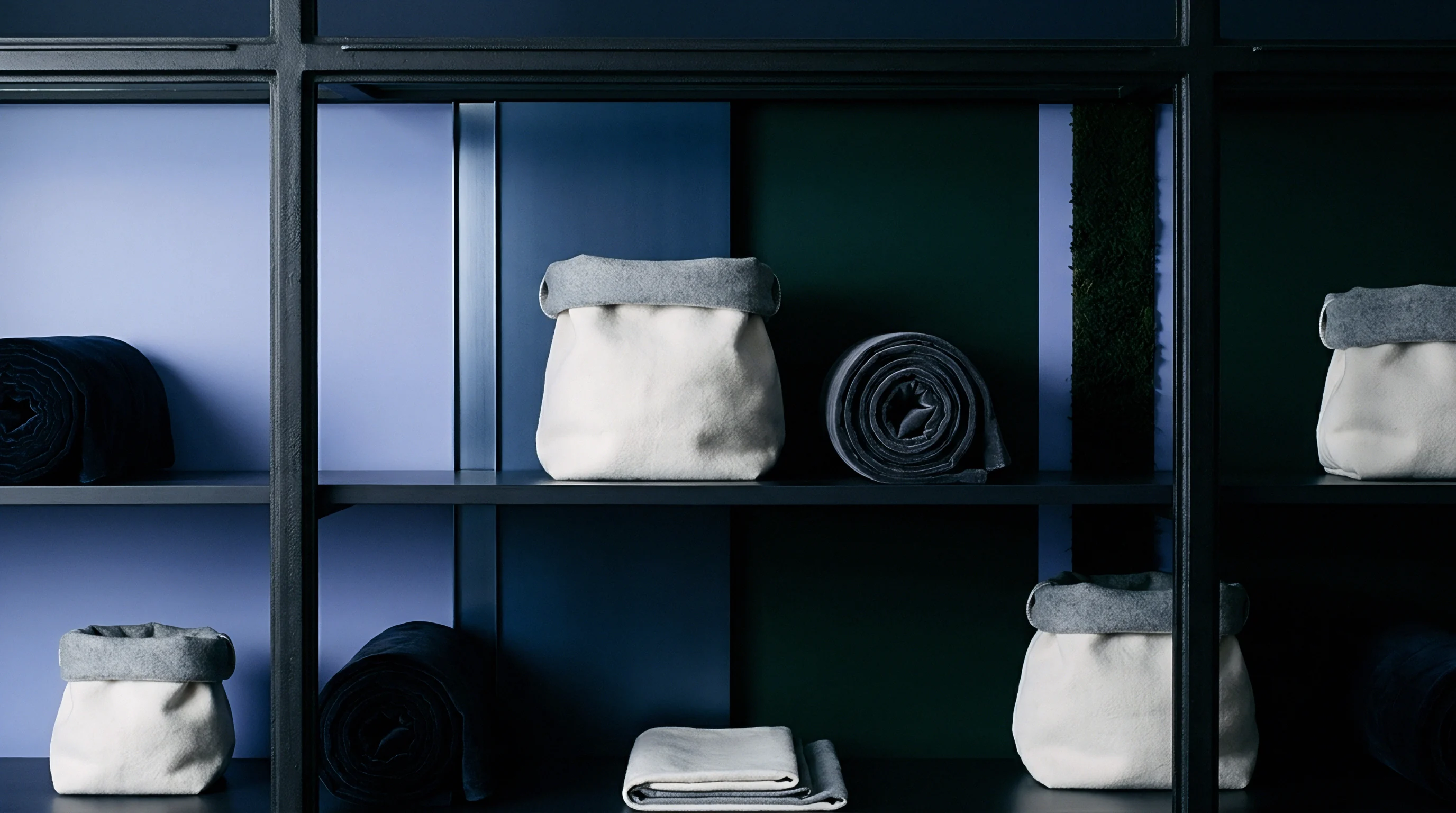 Felt storage containers and tightly rolled fabric bolts rest on the shelves of a dark metal modular shelving system.