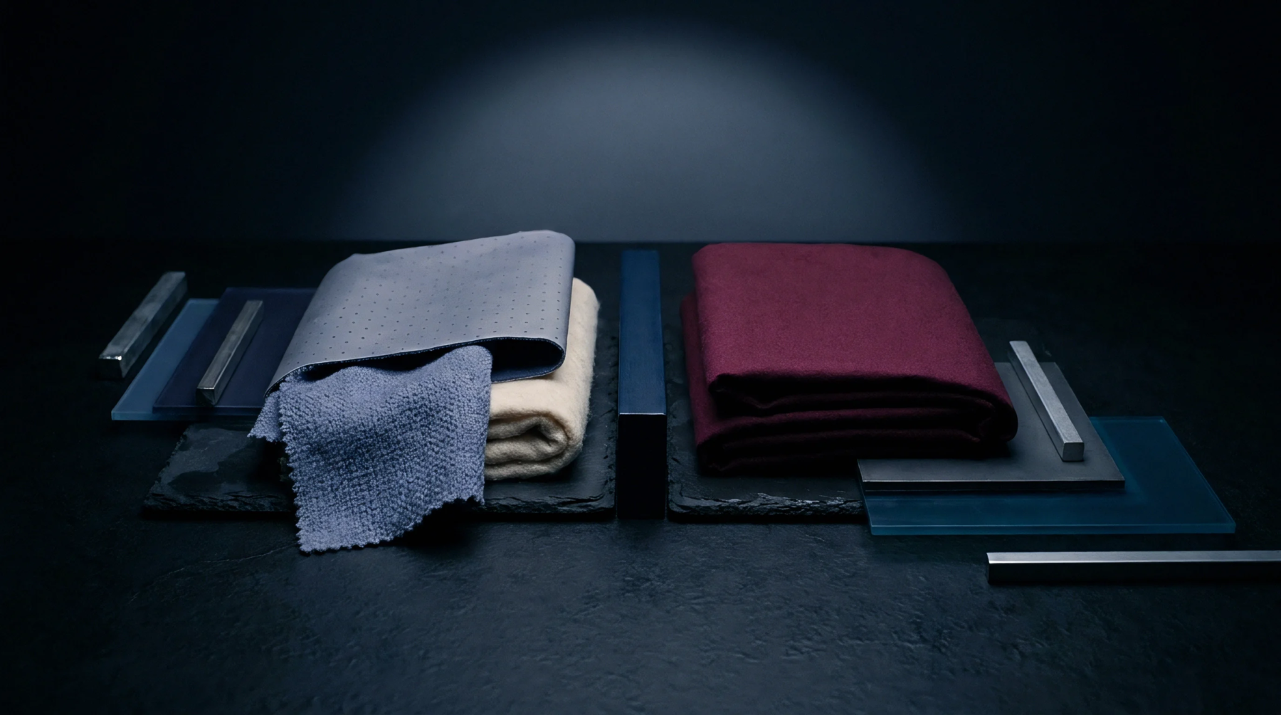 Folded fabric samples including perforated synthetics and woven panels rest upon slate slabs adjacent to rectangular glass elements and brushed metal hardware.